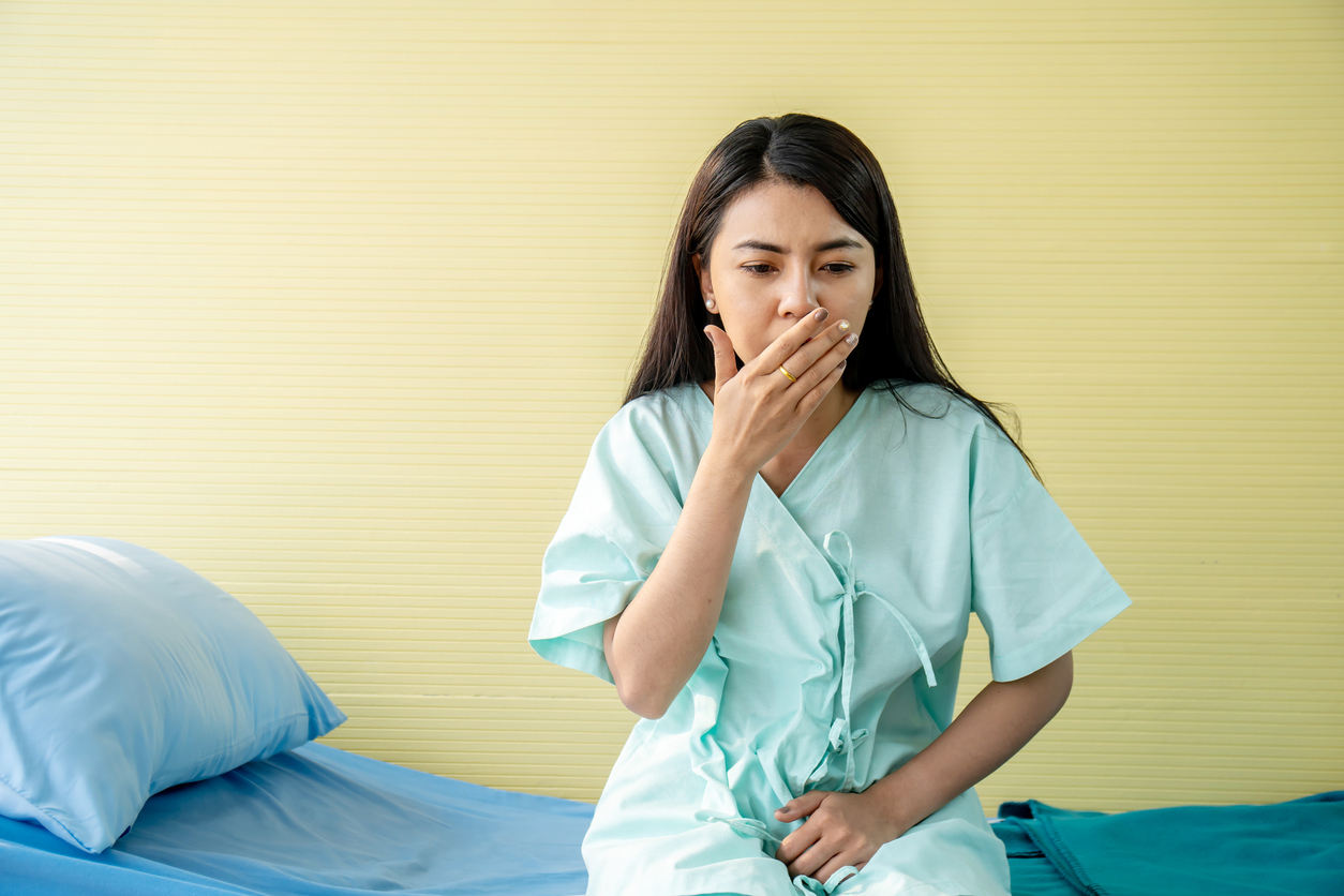 Woman patient suffering from stomach ache and nausea while sitting on bed at hospital, abdominal pain, food poisoning